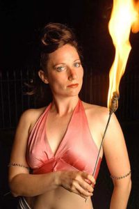 Bex Carney standing with a torch, looking at the camera with an intense gaze.